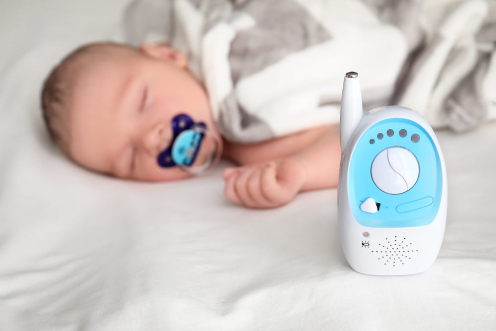 Photo of a sleeping baby with a pacifier right next to a wireless baby monitor