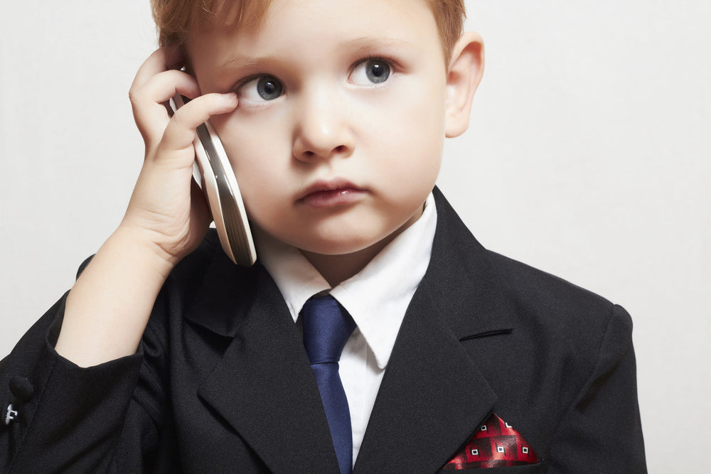 Photo of a little boy in a business suit holding a cell phone up to his head