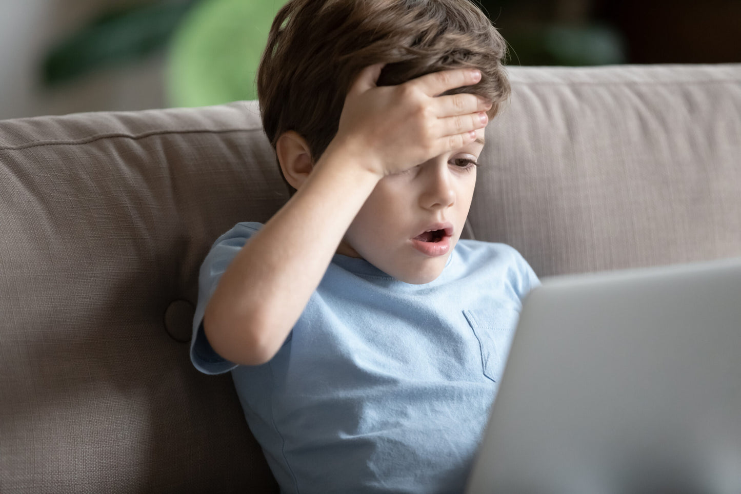 Photo of a young child with a laptop on lap, and shocked look on his face as he looks at the screen
